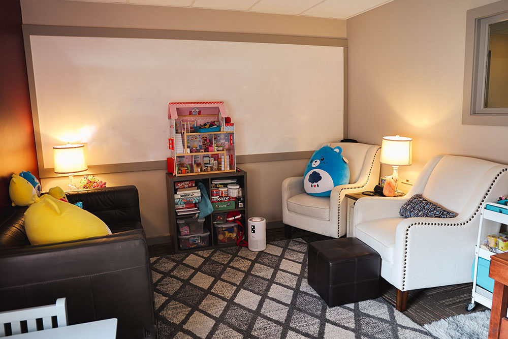 A Your Story Matters Therapy Group office with a couch, two chairs, lamps, and bookshelves